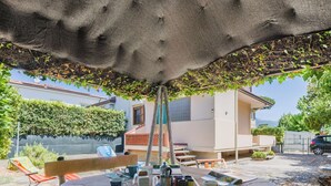 An outdoor dining area with a wooden table set for four, surrounded by a garden with a pergola overhead. - Casa Claudia by Interhome (Lido di Camaiore)