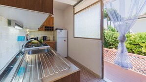 A compact kitchen with a stainless steel sink, wooden cabinets, a refrigerator, and a window with sheer curtains. - Casa Claudia by Interhome (Lido di Camaiore)