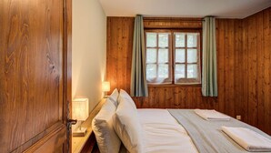 A wooden-paneled room with a bed, a nightstand, a lamp, and a window with curtains.
