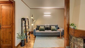 A cozy living room with a grey sofa, a small side table, a floor lamp, and a wooden door.