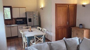 Ein gemütliches Wohnzimmer mit einer Couch, einem Esstisch mit Stühlen, einer Küchenzeile inklusive Kühlschrank und Mikrowelle sowie Holzbalken an der Decke.