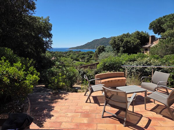A patio with outdoor furniture, a view of the sea, and surrounding greenery.