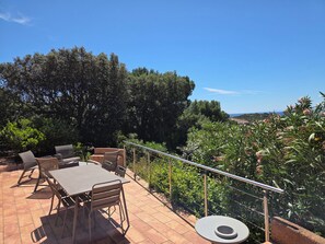 An outdoor patio with a table and chairs, surrounded by greenery and a view of the landscape.