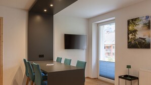 A modern meeting room with a large table, teal chairs, a mounted TV, and a window with a view of buildings. - Superior Apartment with IR-Sauna (No Deposit) (Eisenerz)