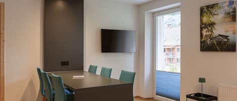 Una sala de reuniones moderna con una mesa grande, sillas color turquesa, un televisor montado y una ventana con vistas a edificios.