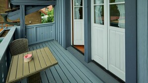 Een overdekt terras met een tafel en stoel, een raam met gordijnen en een houten terras.