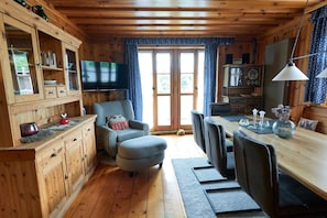 L’intérieur d’un chalet en bois comprend une télévision, une table à manger, des chaises et un coin salon confortable.