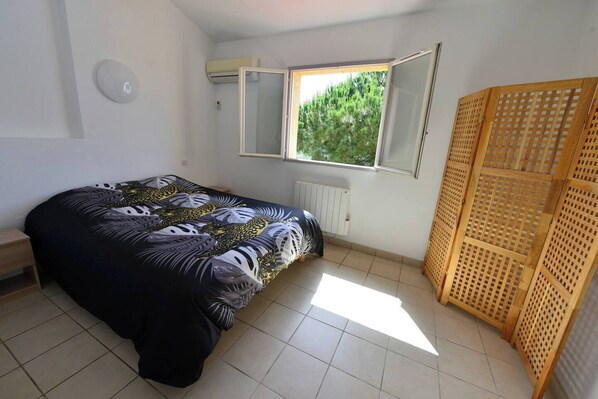 Ein Schlafzimmer mit Bett, Fenster, Heizkörper und einer Holzwand.