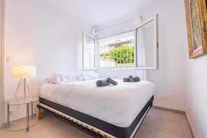 Quarto com cama, luminária de cabeceira, janela com vista e espelho fixado na parede.