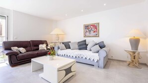 A modern living room with a brown leather sofa, a white coffee table, a grey sofa, and a decorative sculpture on a pedestal. - Apartment Near the Sea – Valras-Plage (Valras-Plage)