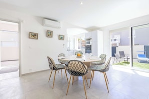 Uma sala de jantar moderna com uma mesa redonda, seis cadeiras estampadas, teto branco e vista para um jardim através de portas de vidro.