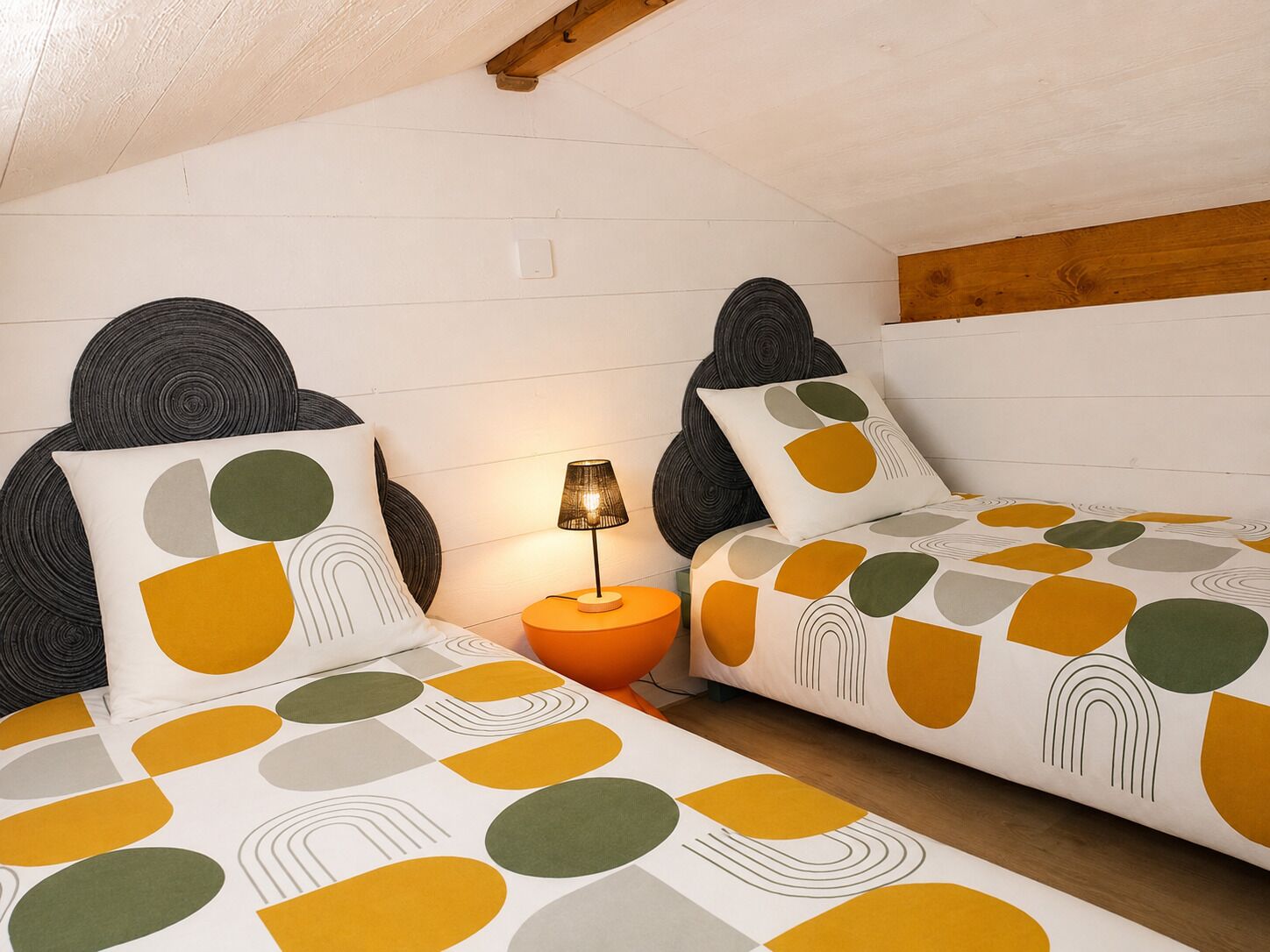 A room with two beds, a nightstand, a lamp, and a wooden ceiling beam.