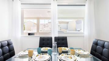 Une table à manger pour quatre personnes, avec des chaises noires, un plateau en verre transparent et des assiettes à motifs floraux.