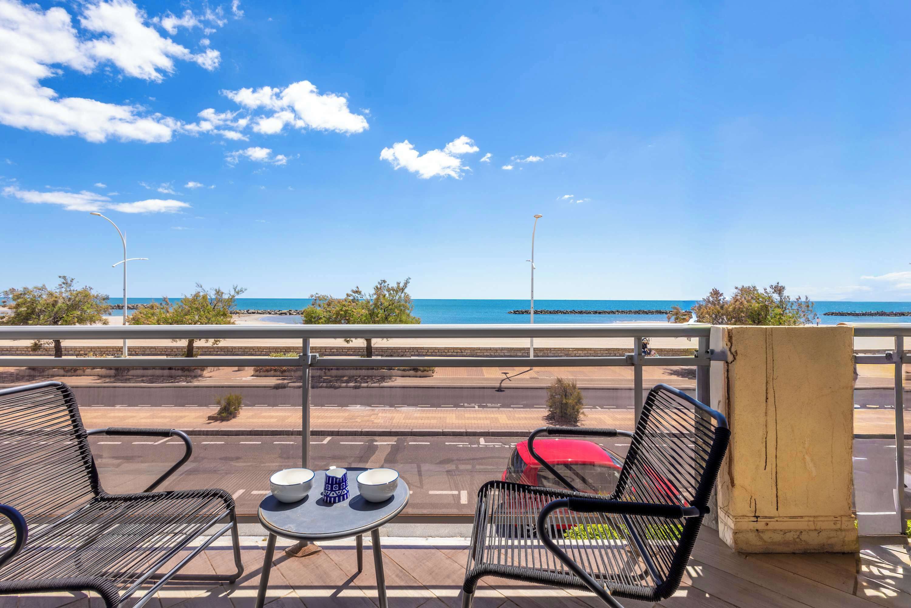 Un balcon avec deux chaises, une petite table et une vue sur l’océan et la route.