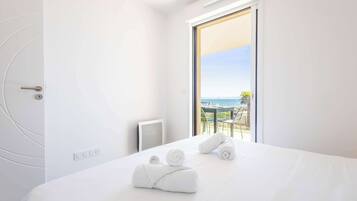 A hotel room with a bed, a view of the sea, and a balcony with a table and chairs.