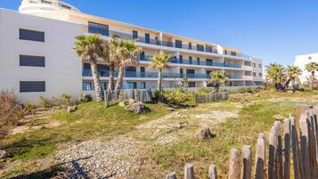 A multi-story hotel with balconies, a grassy area with palm trees, and a wooden fence.
