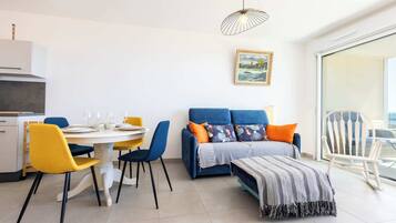 A modern living room with a dining area, a sofa, a rocking chair, and a large window.