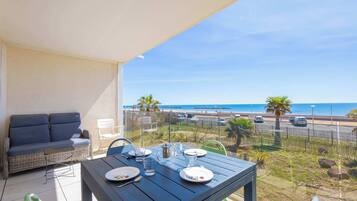 A balcony with a table set for two, overlooking a beach and a road.