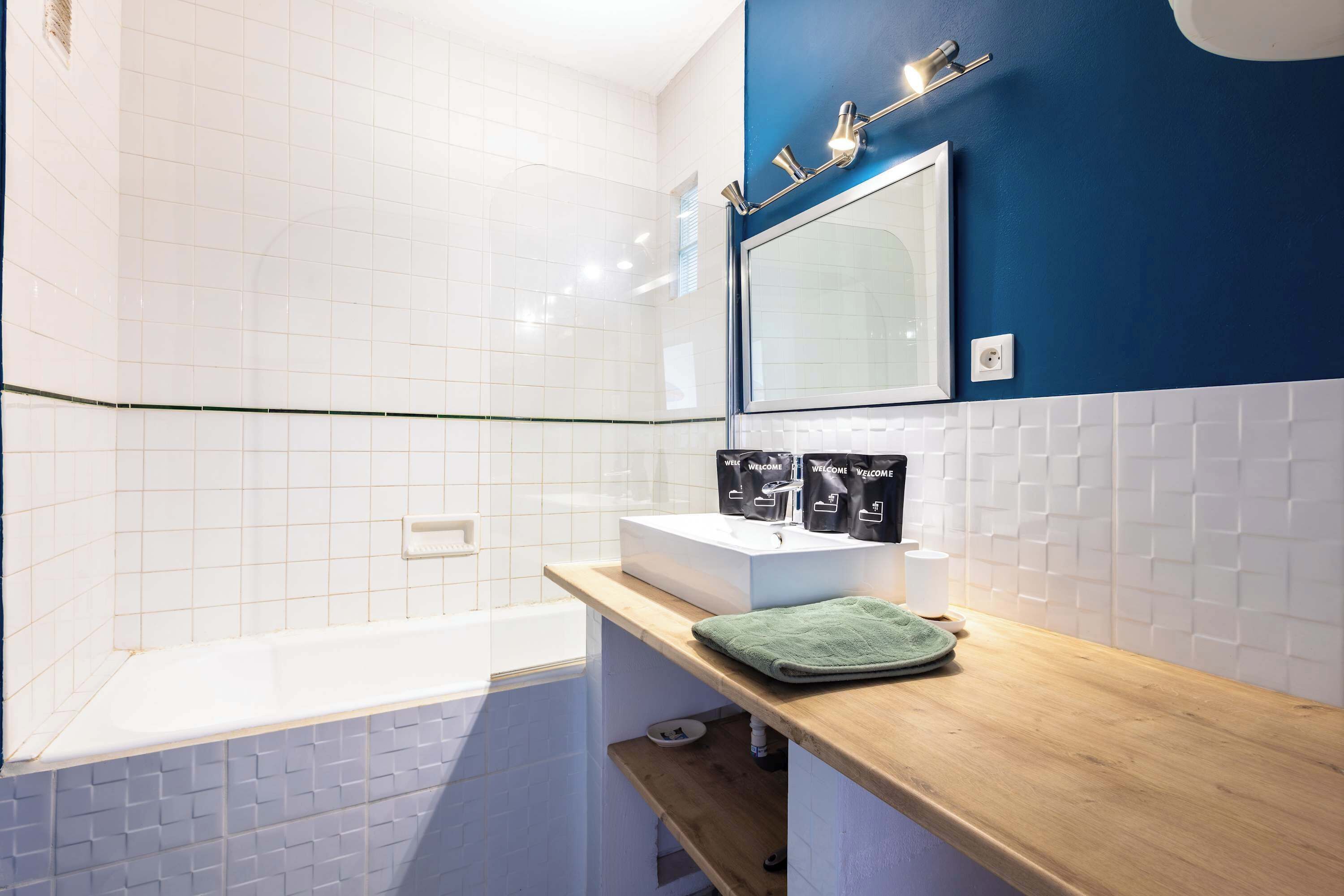 A bathroom with a bathtub, a sink with a mirror, and a shelf with toiletries.