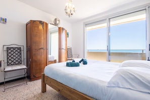Quarto com cama, guarda-roupa, uma cadeira e uma janela grande com vista.