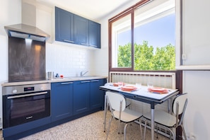 Uma cozinha com forno Bosch, armários azuis, janela com vista para árvores e uma mesa de jantar com cadeiras.