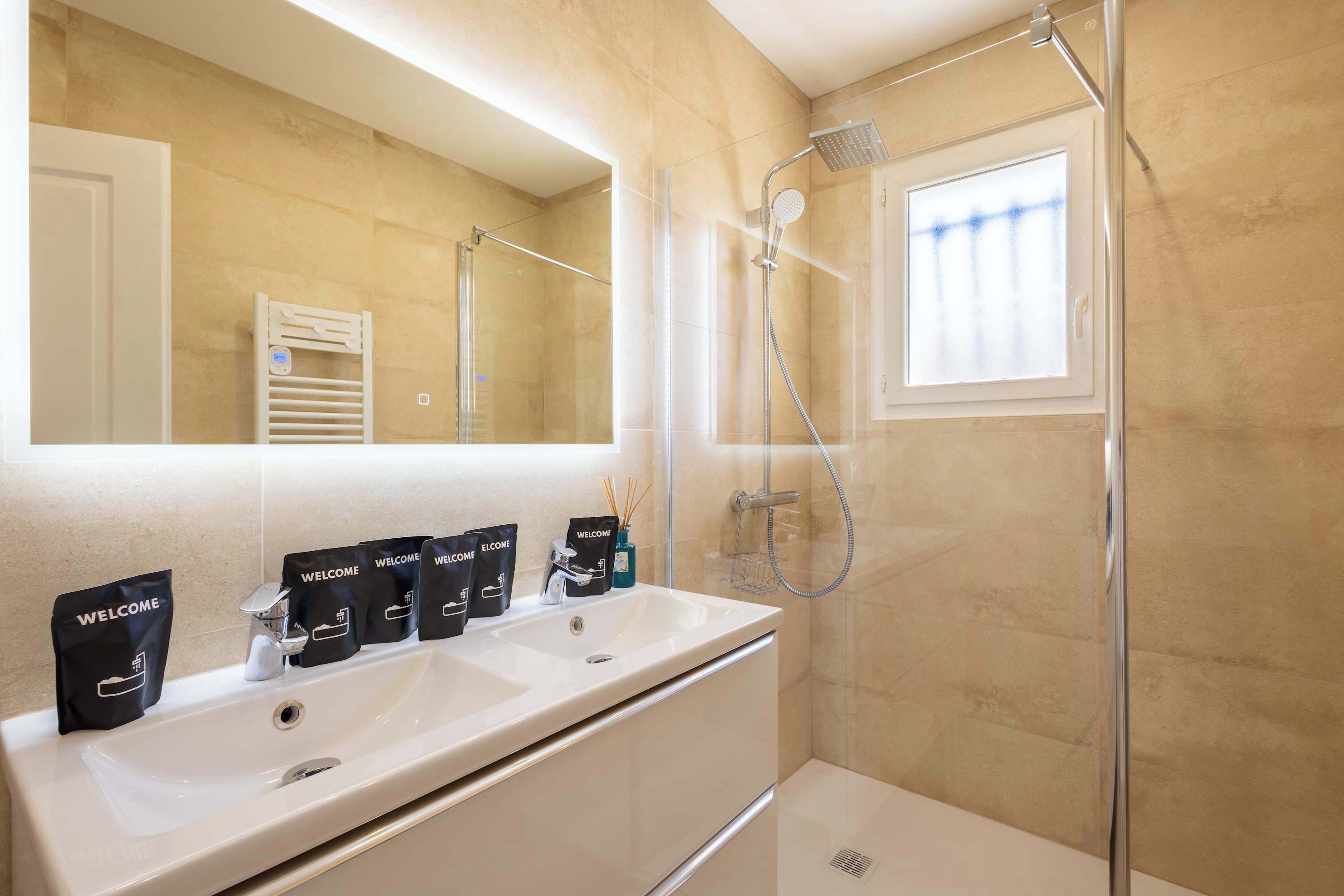 Un baño con dos lavamanos, ducha, toallero y ventana.