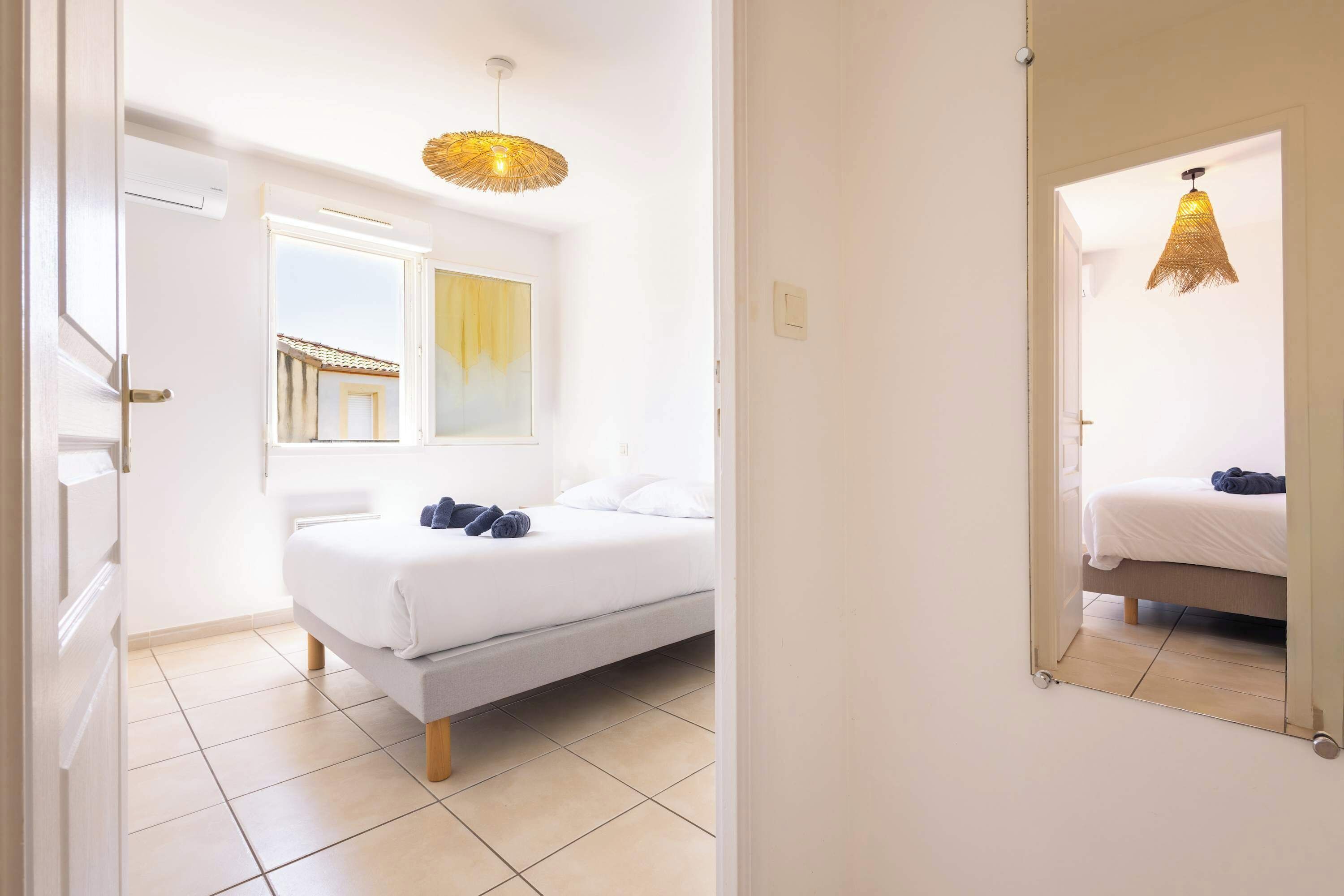 A bedroom with a bed, a window, a wall-mounted light fixture, and a mirror.
