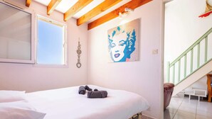 A bedroom with a bed, a window, a painting, and a staircase. - La Parenthese au Sud · Valras'Loc (Valras-Plage)