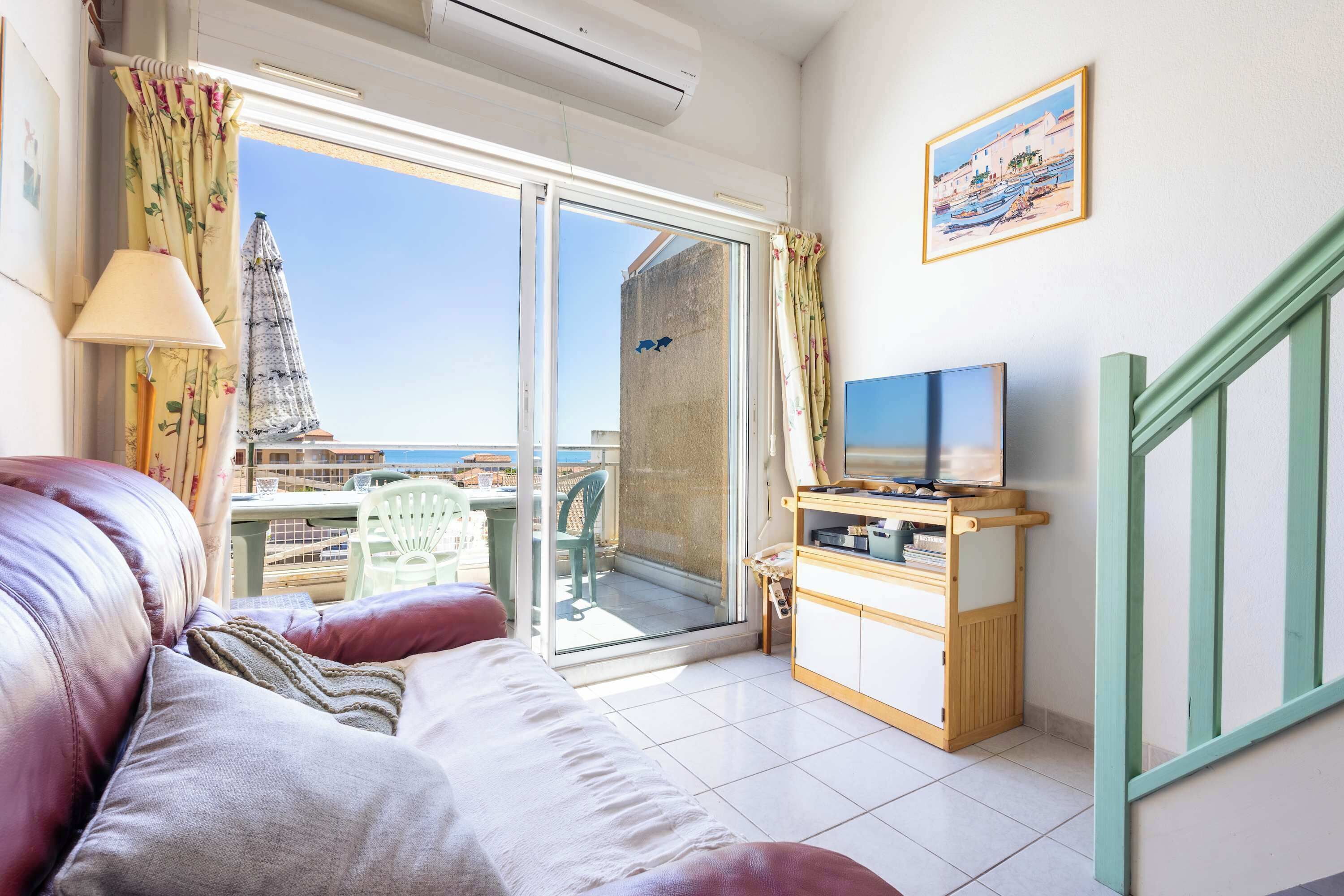 Un balcon avec vue sur la mer, un canapé, un meuble pour la télévision et une lampe.