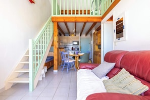 Una escalera conduce a una zona de cocina con una mesa y sillas, un sofá de cuero rojo y un techo de madera.