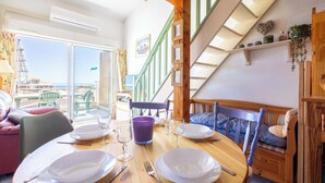 A dining area with a table set for four, a purple candle, and a view of the sea through large windows. - La Parenthese au Sud · Valras'Loc (Valras-Plage)