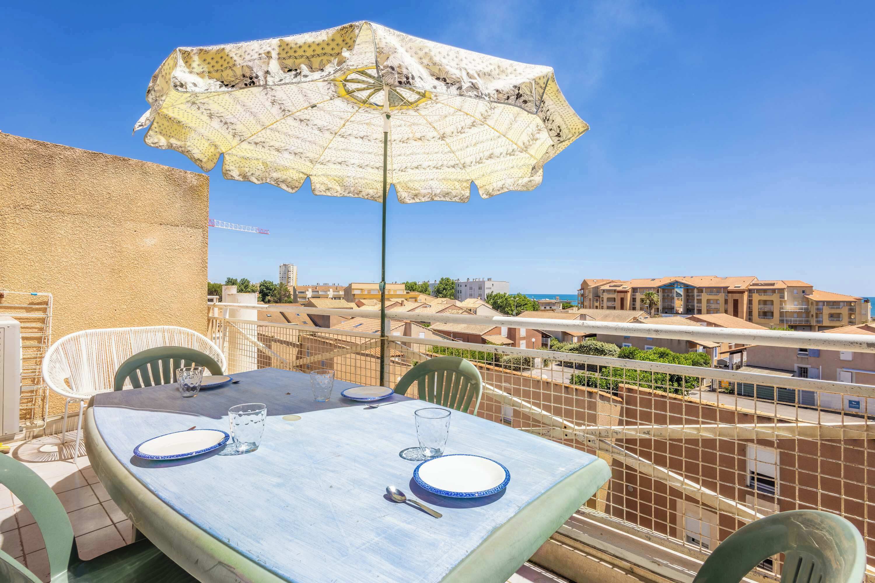 Un balcón con mesa para dos, una sombrilla estampada y vistas de edificios al fondo.
