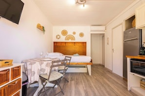 Une pièce de taille modeste comprenant un lit, une petite table avec des chaises, un téléviseur, un réfrigérateur et une tête de lit en bois.