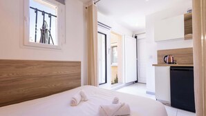 A hotel room with a wooden headboard, a bed with white linens, a window with a view of the outside, and a kitchenette with a coffee maker.