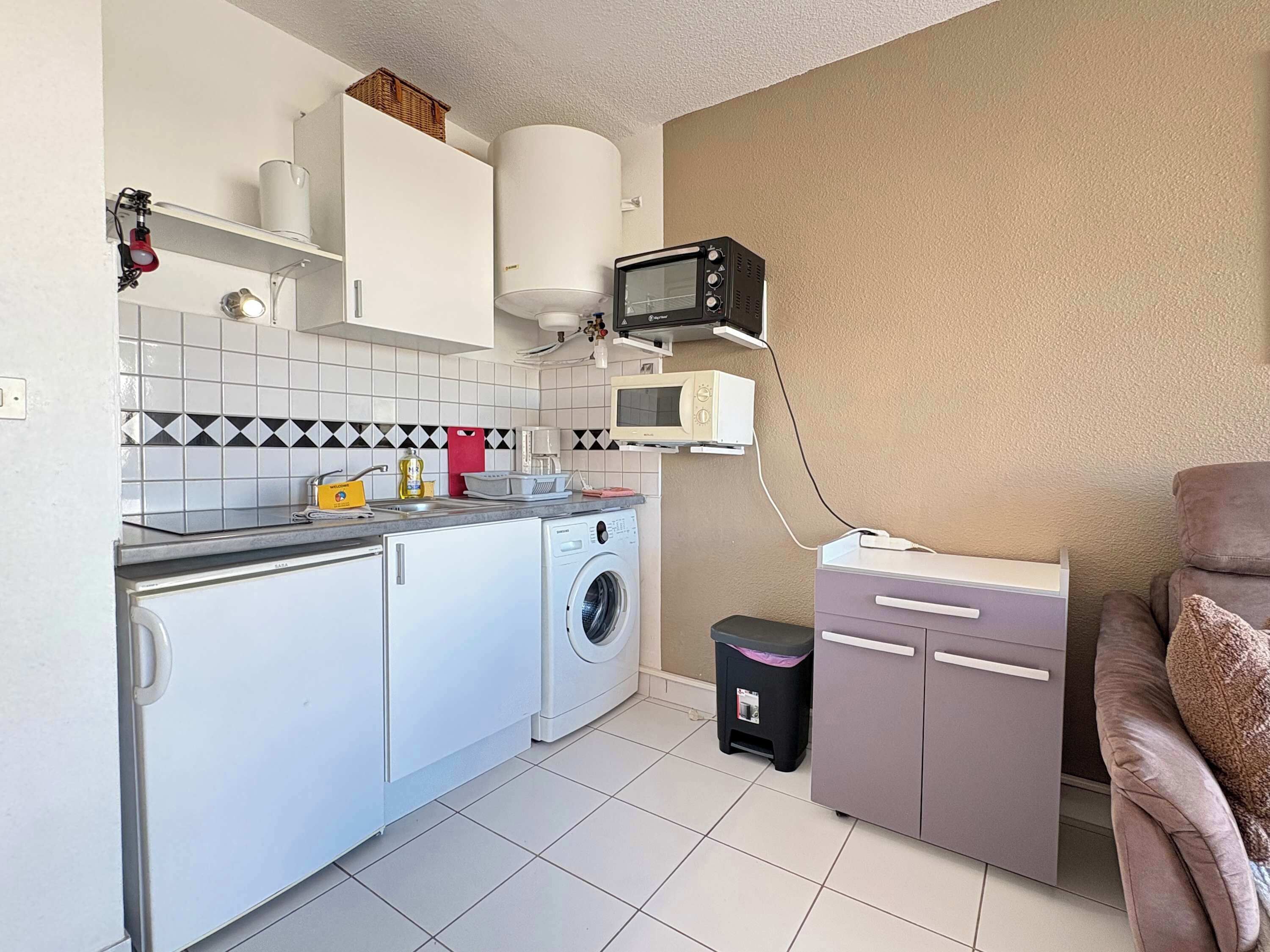 Une cuisine compacte équipée d’un lave-linge, d’un four à micro-ondes et d’un petit placard.