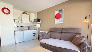 Un espace de vie compact comprenant un coin cuisine, un canapé, une table basse et une horloge murale.