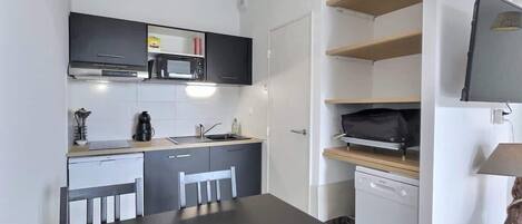 Una cocina compacta con comedor, microondas, cafetera y lavavajillas.