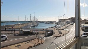 A marina with boats docked, a road with vehicles, and buildings in the background. - Comfortable Studio with Harbour View (Valras-Plage)