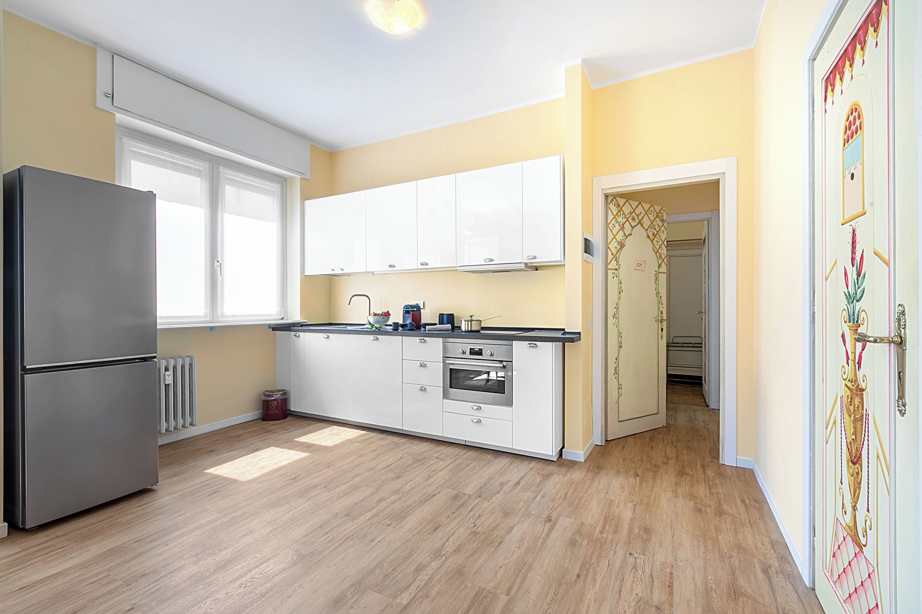 Eine moderne Küche mit weißen Schränken, einem Edelstahlkühlschrank und Holzboden.