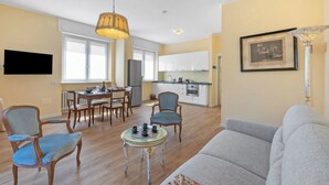 A living room with a sofa, chairs, a dining table, and a kitchen in the background. - Strixia Apartment - 50m From Lake With Balcony (Stresa)
