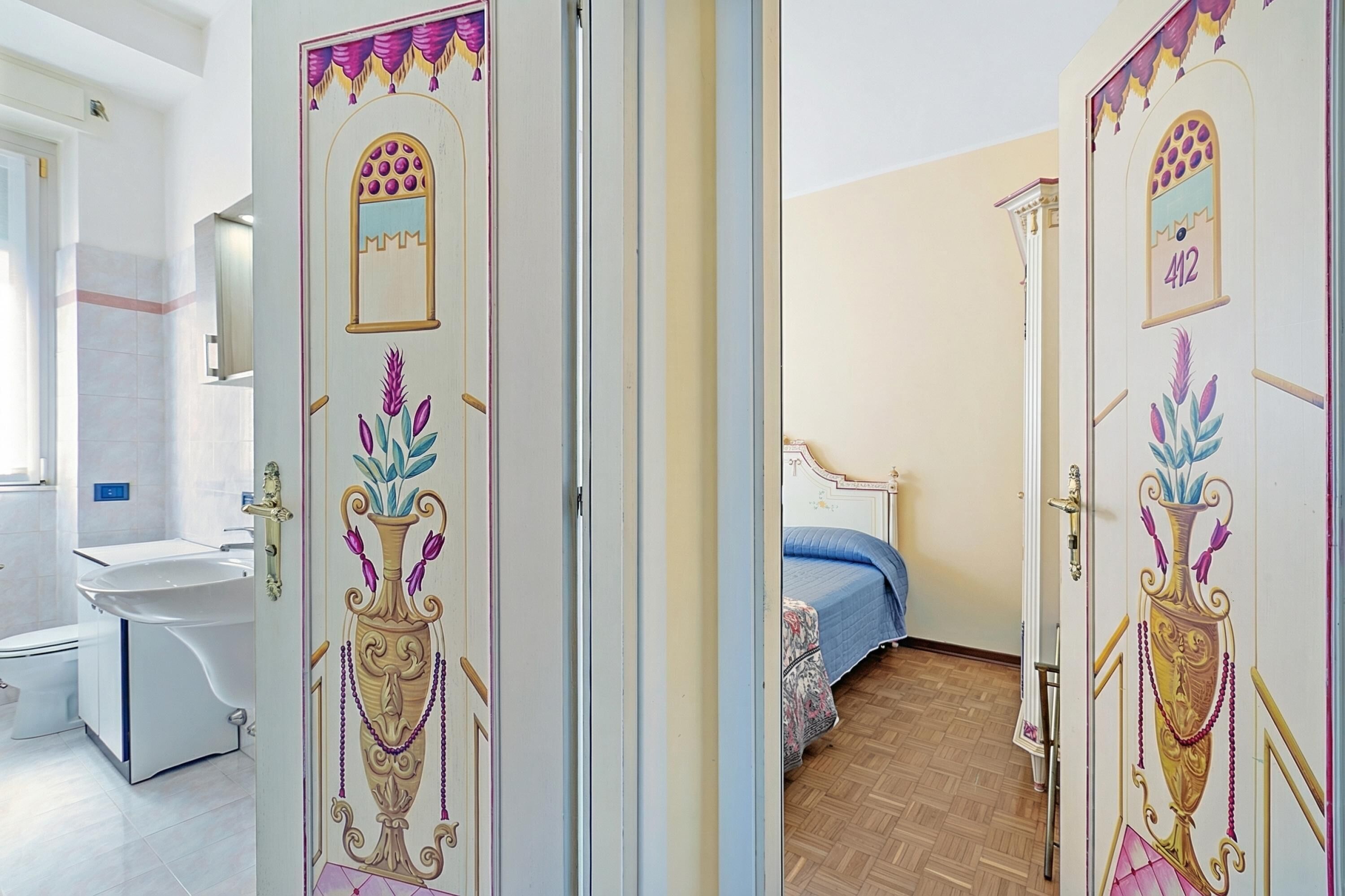 Una habitación con una cama, una mesita de noche, un espejo y una puerta con detalles decorativos.