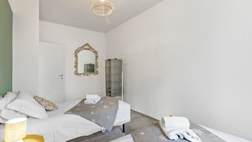 A hotel room with two beds, a large mirror, a hanging light fixture, and a wardrobe.