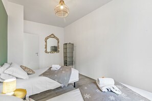 A hotel room with two beds, a large mirror, a hanging light fixture, and a wardrobe.