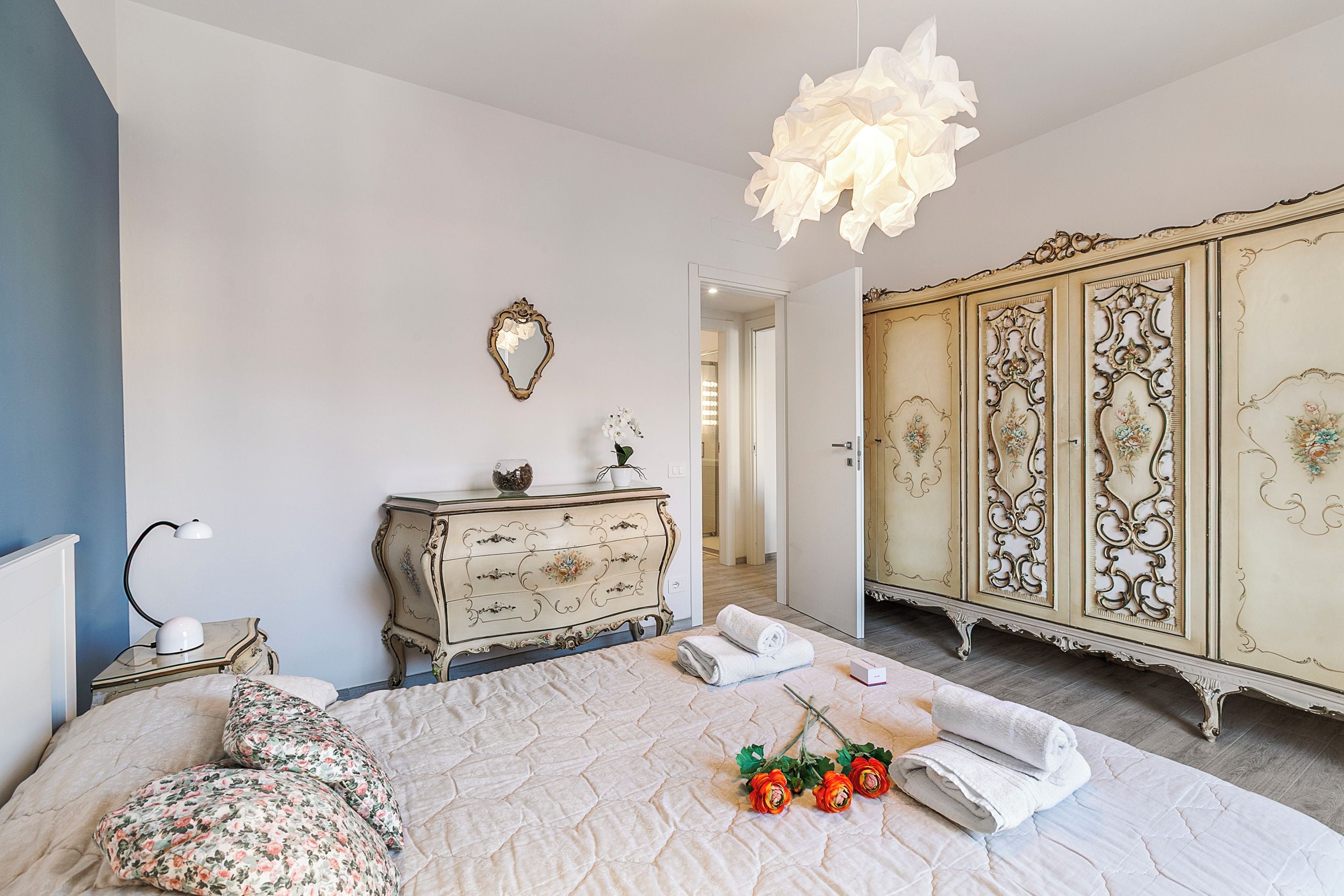 A bedroom with a bed, a dresser, a mirror, and a chandelier.