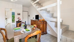 A dining area with a wooden table set for four, a staircase with a white railing, and a view of a balcony with plants. - Incanto Del Lago 50m to Lake Maggiore (Baveno)