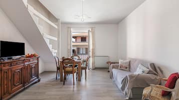 Un vaste espace de vie comprenant une table à manger, des chaises, un canapé et un téléviseur posé sur un meuble en bois.