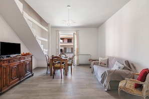 Amplia sala de estar con mesa de comedor, sillas, un sofá y un televisor sobre un mueble de madera.