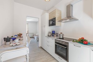 Una cocina moderna con armarios blancos, horno empotrado, microondas y cafetera.