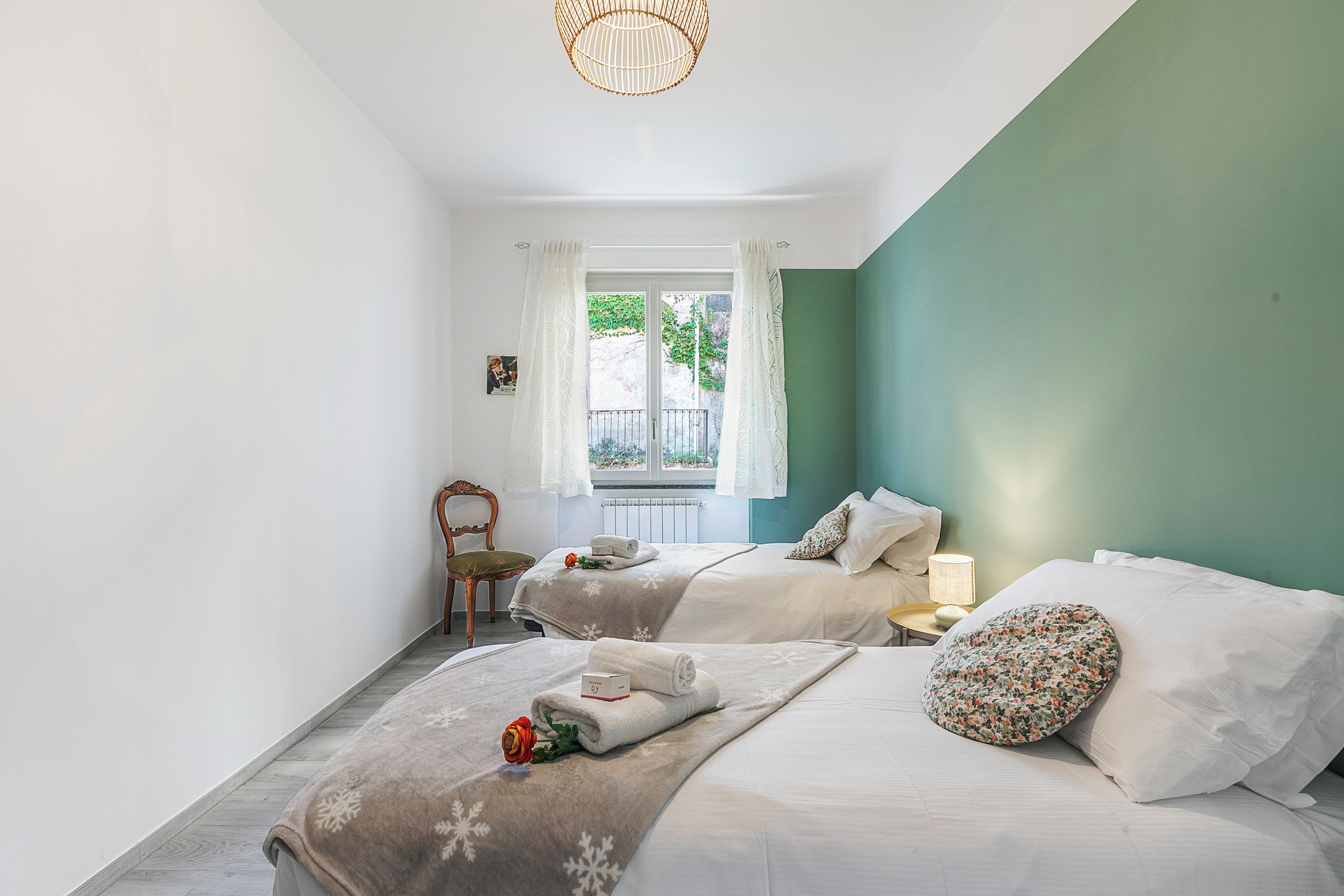 Une chambre avec deux lits, une fenêtre avec des rideaux, une chaise et une table de chevet avec une lampe.