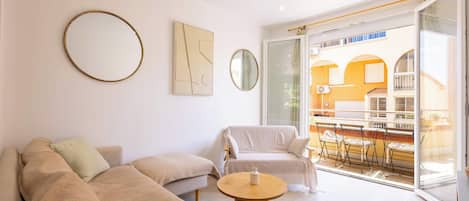 A living room with a sofa, armchairs, a round coffee table, and a balcony with outdoor furniture.